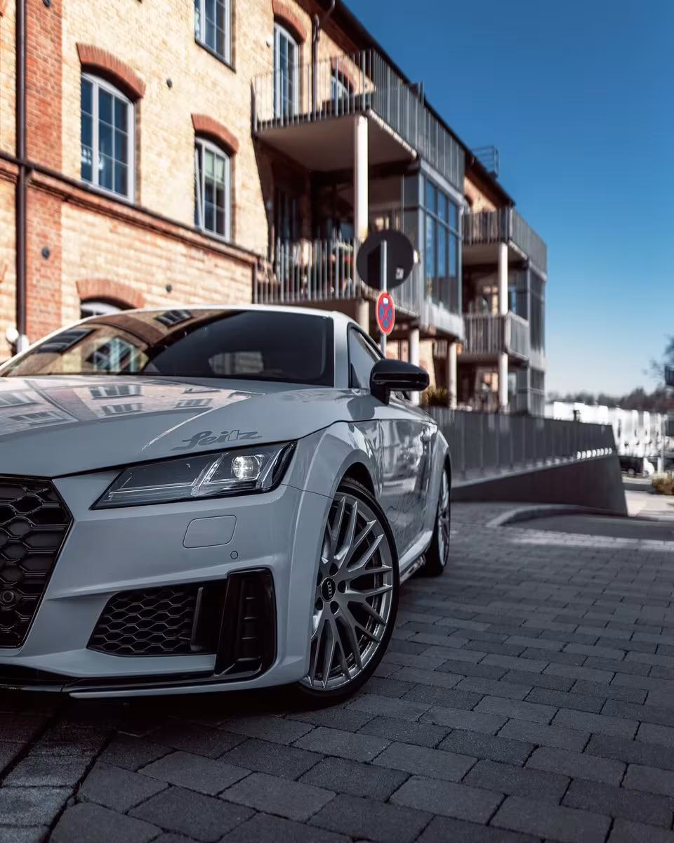 Grauer Audi TT mit „Feitz“-Schriftzug vor einem Backsteinhaus auf Kopfsteinpflaster.