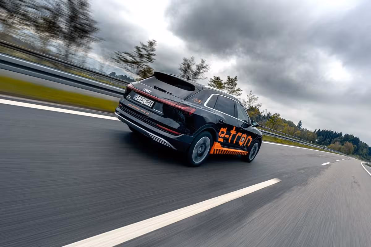 Black Audi e-tron with orange lettering driving on a highway.