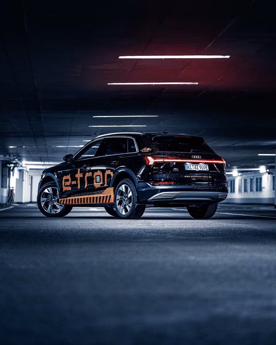 Black Audi e-tron with orange vinyl wrap in a lit underground parking garage.