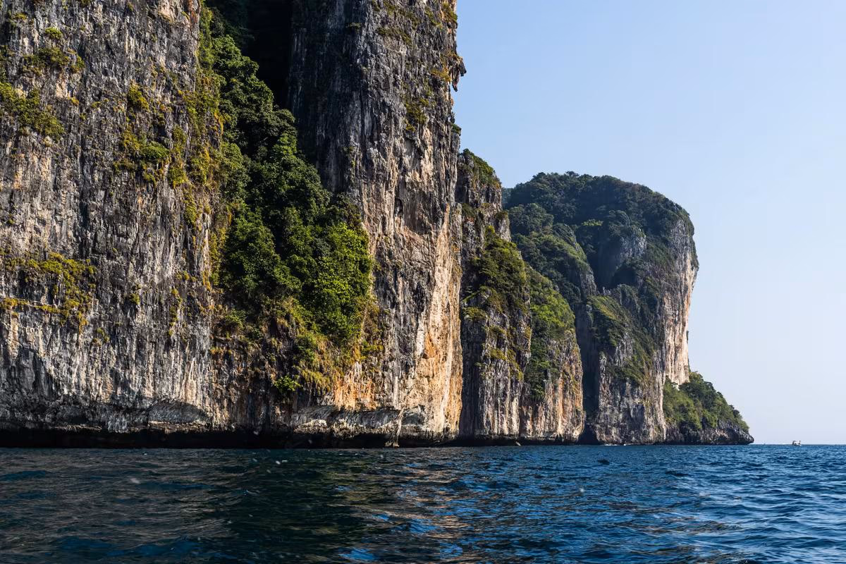 Thailand: Steile, bewachsene Klippen am Meer unter klarem Himmel