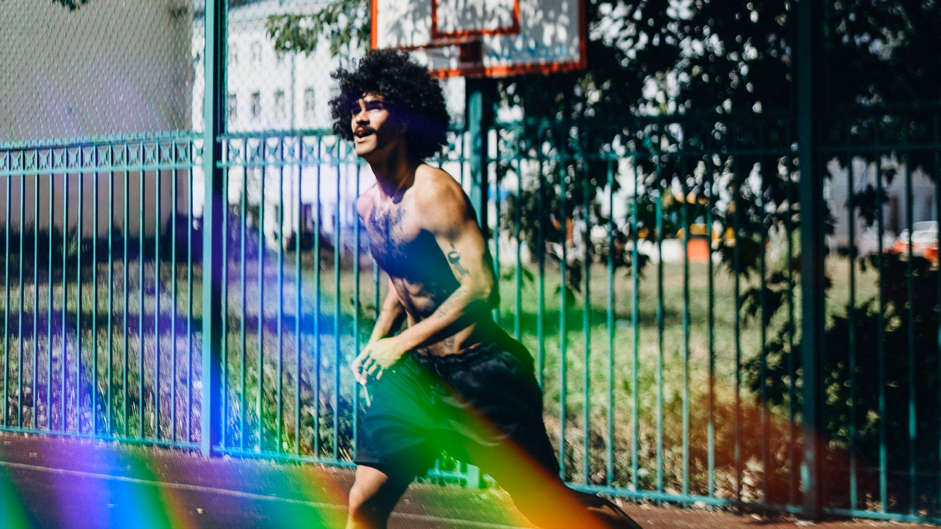 Hemdsloser Mann mit Afro-Haaren rennt auf einem Sportplatz vor grünem Zaun.