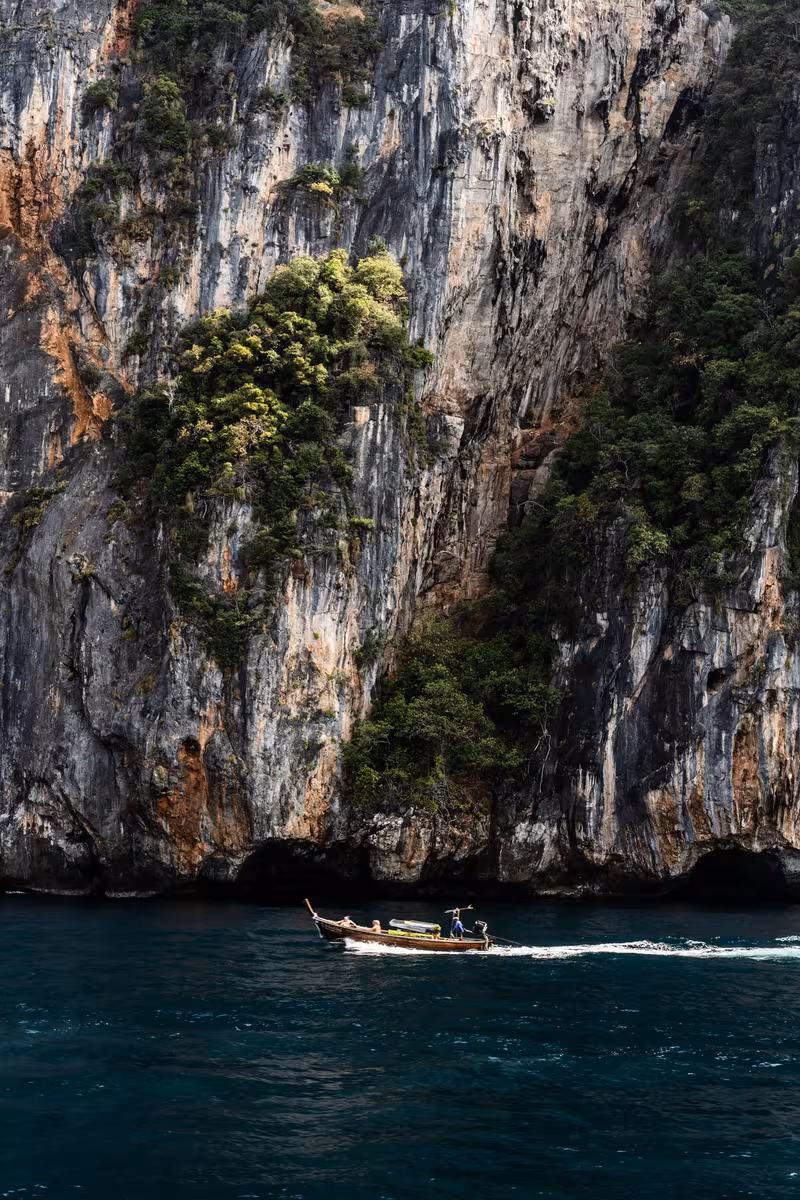 Thailand: Langschwimmboot vor steiler, bewachsener Kalksteinfelswand im Meer