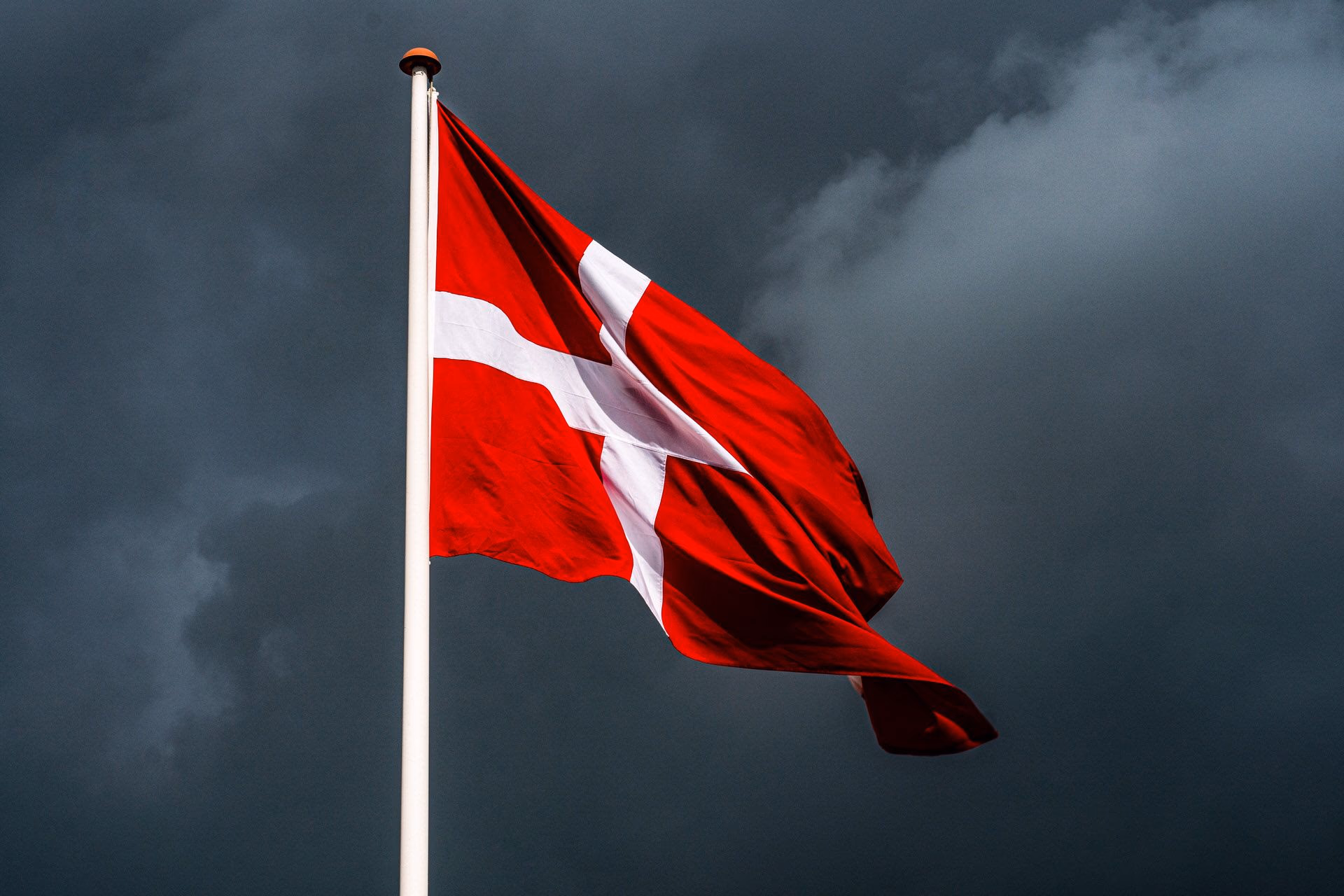 Danish flag waving against a dark, cloudy sky.