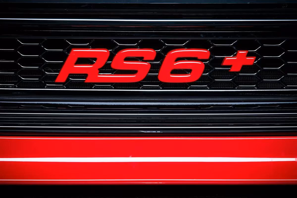 ABT: Rotes RS6+-Emblem auf schwarzem Wabenrost eines ABT Sportsline Fahrzeugs.