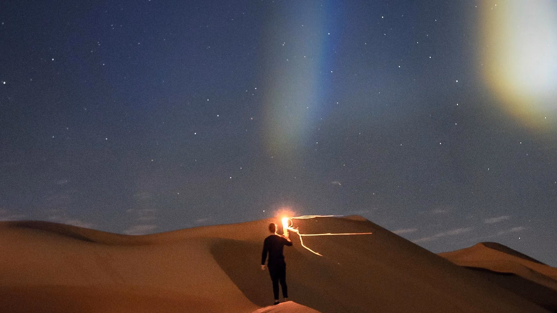 Person mit Lichtmalerei auf Düne unter Sternenhimmel