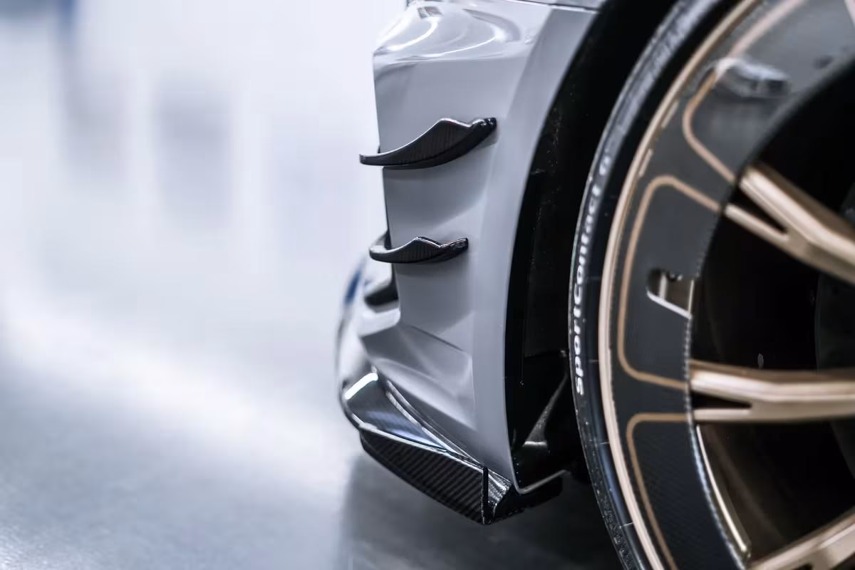 Audi: Detailansicht eines grauen Sportwagens mit Carbon-Elementen und goldfarbener Felge.