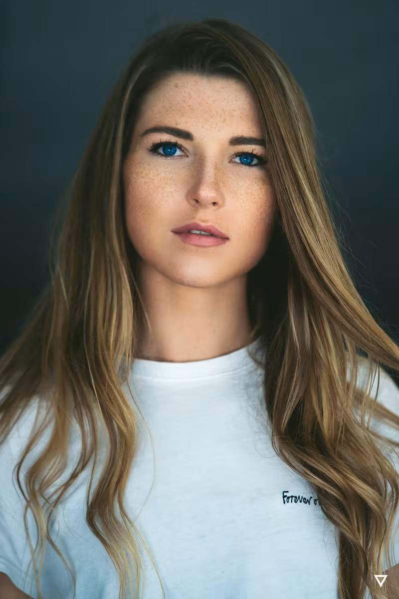Lifestyle: Porträt einer jungen Frau mit blonden Haaren und weißem T-Shirt vor dunklem Hintergrund.