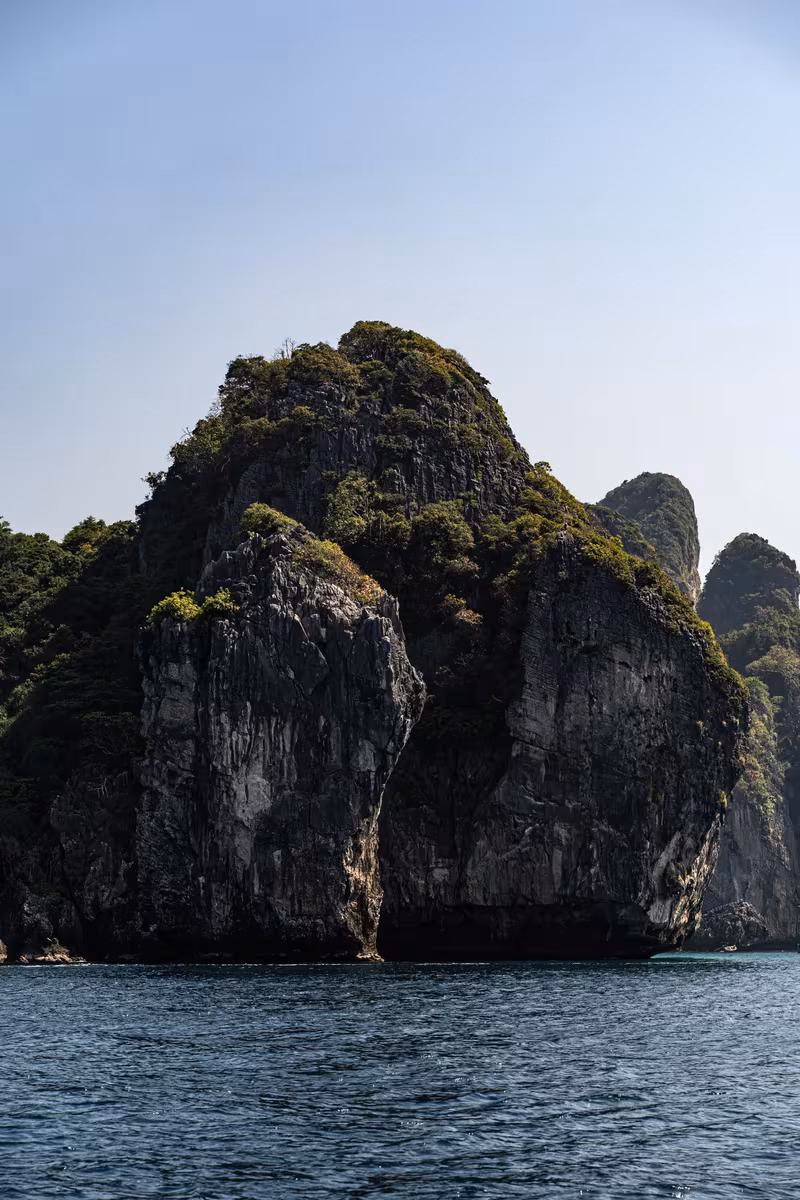 Thailand: Steile, bewachsene Felsklippe, die aus dem Meer aufragt.
