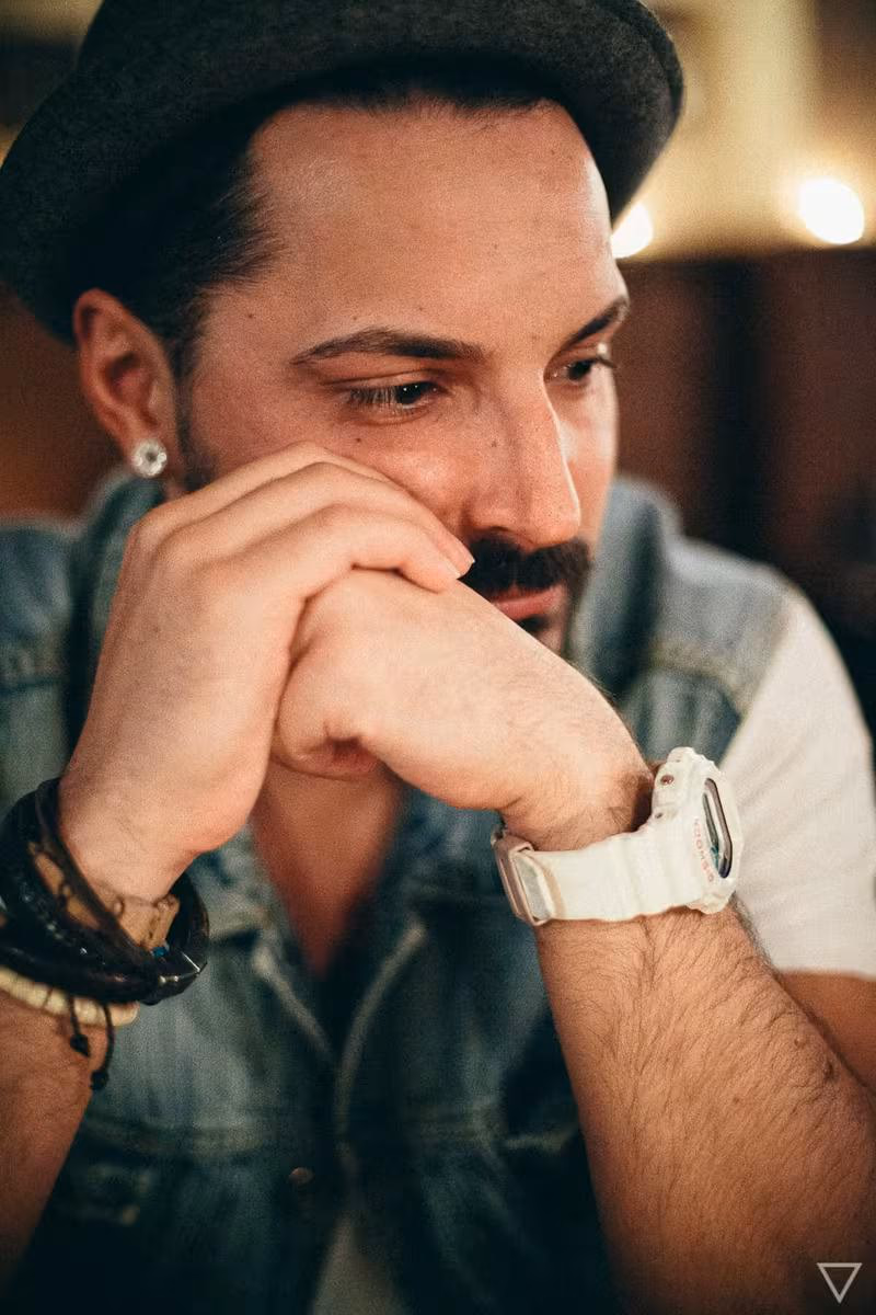 Lifestyle: Mann mit Hut und Bart, Hände vor dem Gesicht, weiße Uhr am Handgelenk.