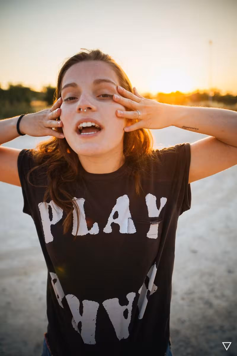 Lifestyle: Frau mit schwarzem T-Shirt mit weißem Aufdruck „PLAY“ bei Sonnenuntergang