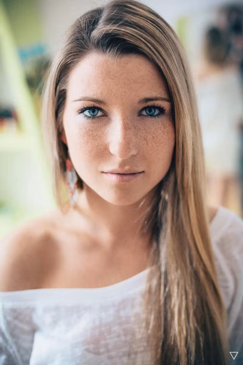 Lifestyle: Porträt einer jungen Frau mit blonden Haaren und Sommersprossen in weißem Oberteil.