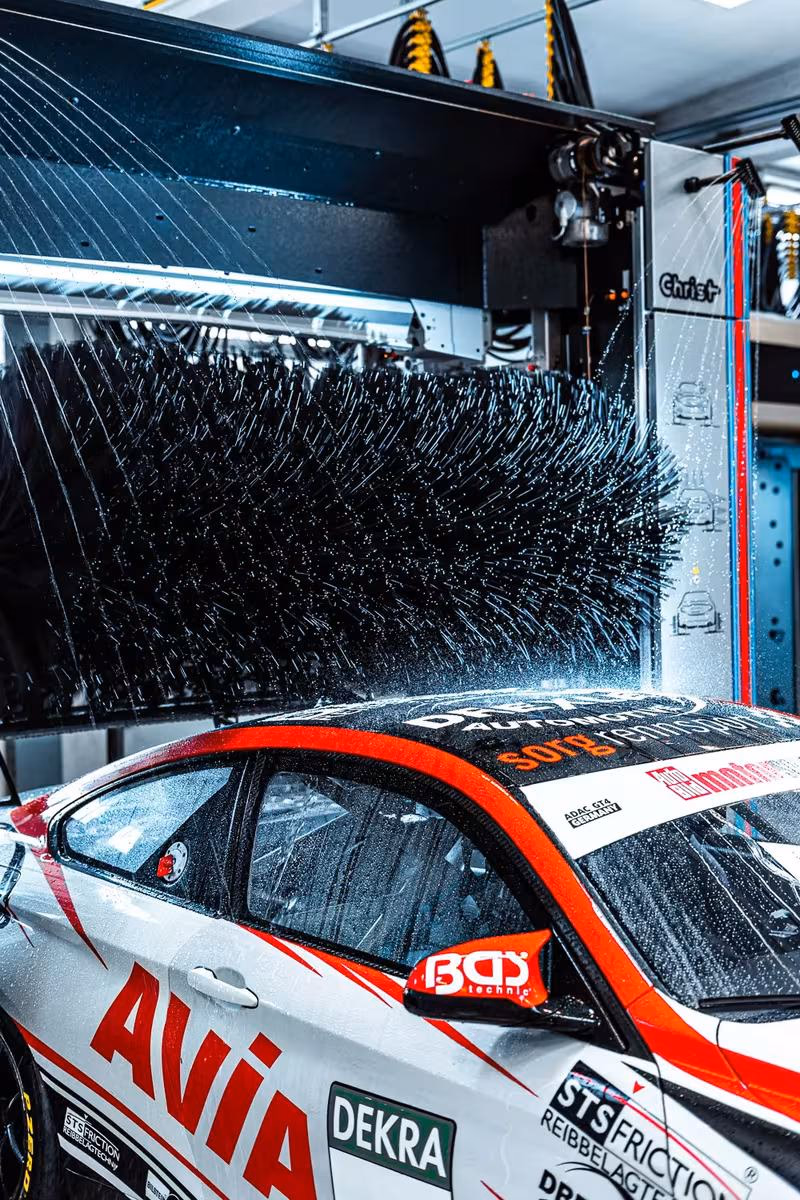 Rennwagen mit Sponsorenlogos wird in einer Christ-Waschanlage mit rotierenden Bürsten gereinigt.