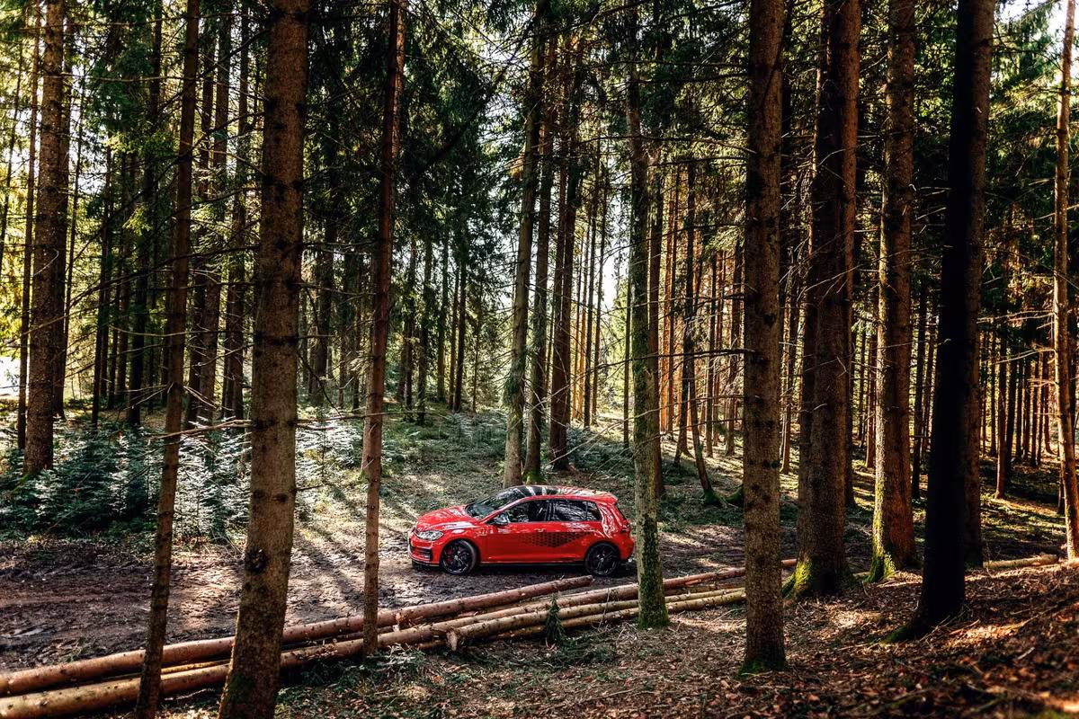 Volkswagen: Roter VW Golf GTI fährt auf einem Waldweg durch den Allgäuer Nadelwald.