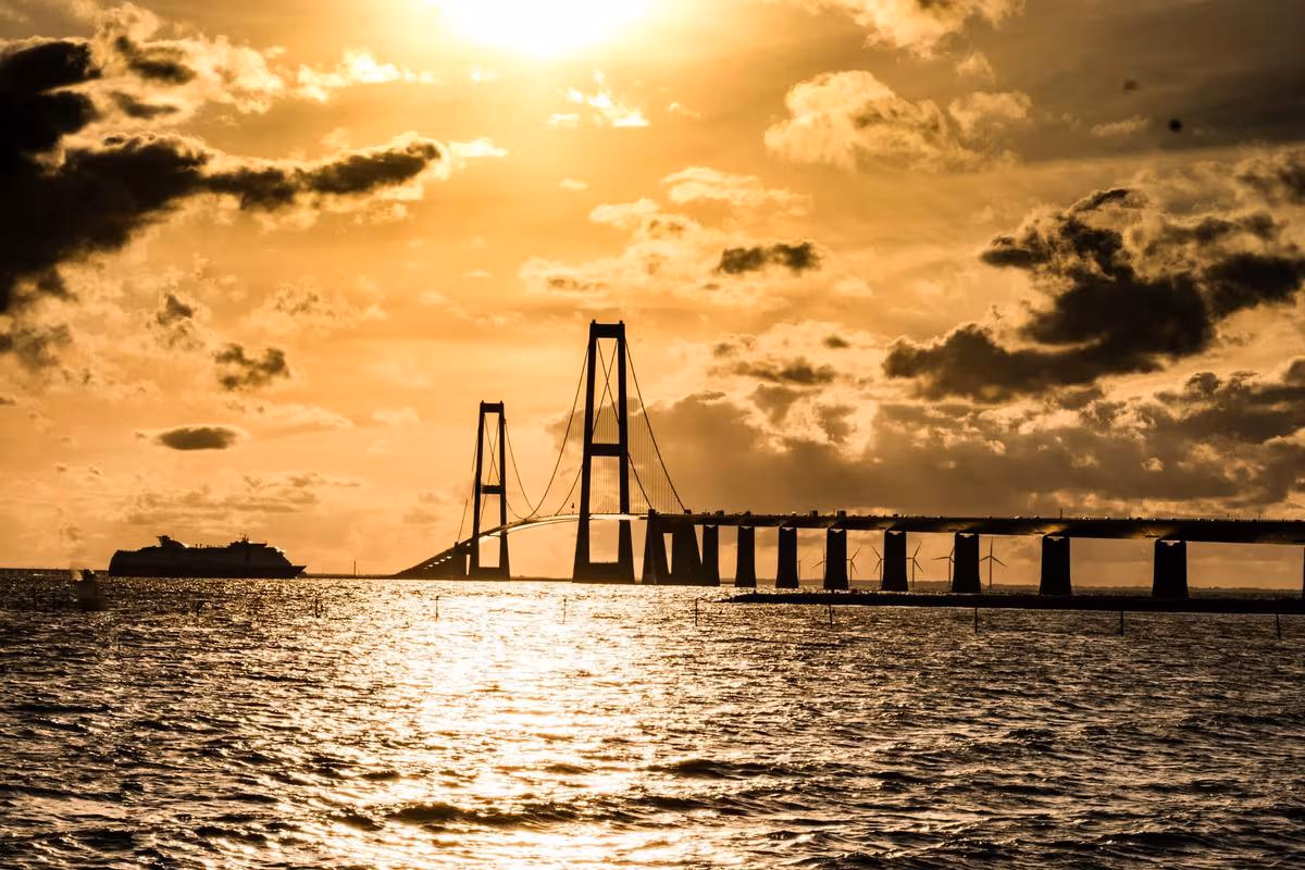 Copenhagen: Silhouette einer Hängebrücke und eines Schiffes auf dem Meer bei goldenem Sonnenuntergang.