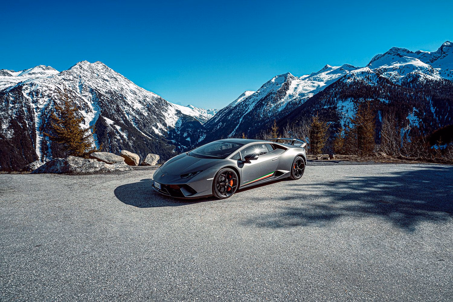 Grauer Lamborghini Huracán auf asphaltierter Fläche vor schneebedeckten Bergen