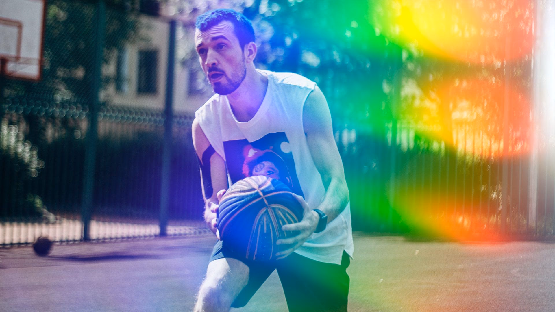 Mann mit Basketball auf dem Platz, starkes Regenbogen-Lichtleck im Bild.