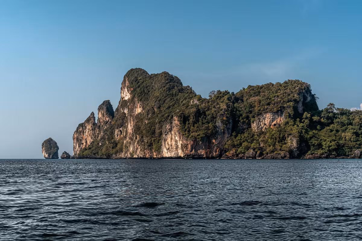 Thailand: Felsige, bewaldete Insel im Meer unter blauem Himmel