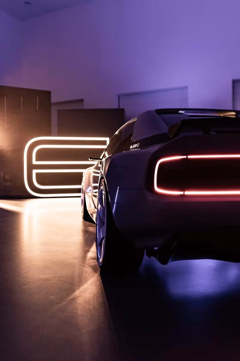 E-Legend: Sportwagen mit roten LED-Leuchten vor leuchtendem Neon-Logo in dunklem Raum