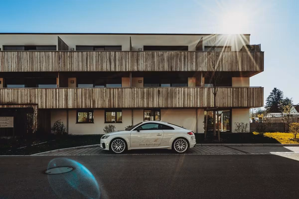 Weißer Audi TT vor modernem Holzgebäude mit „Ihre Autohaus“ Schriftzug