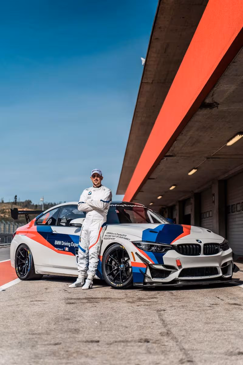 Rennfahrer in weißem Overall neben BMW M4 GT3 im BMW Driving Experience Design.