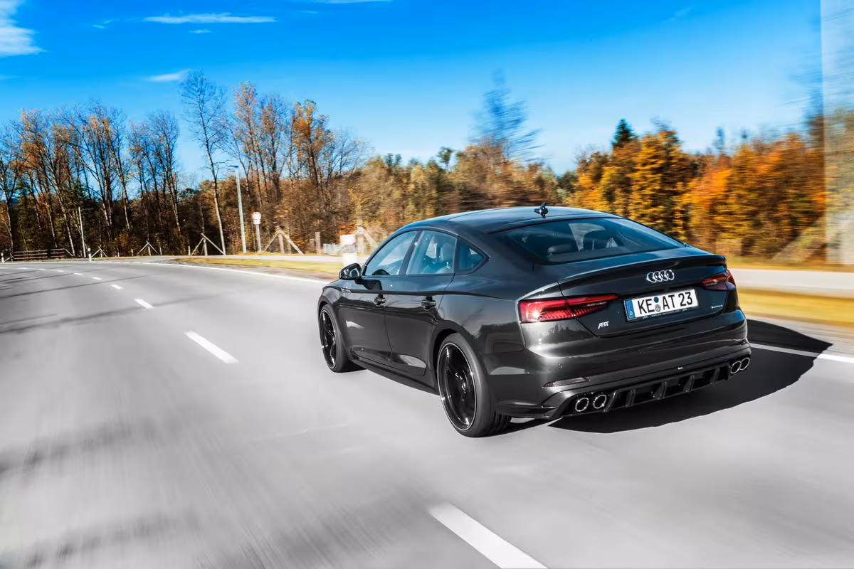 Schwarzer Audi RS7 fährt auf Landstraße durch herbstliche Landschaft.