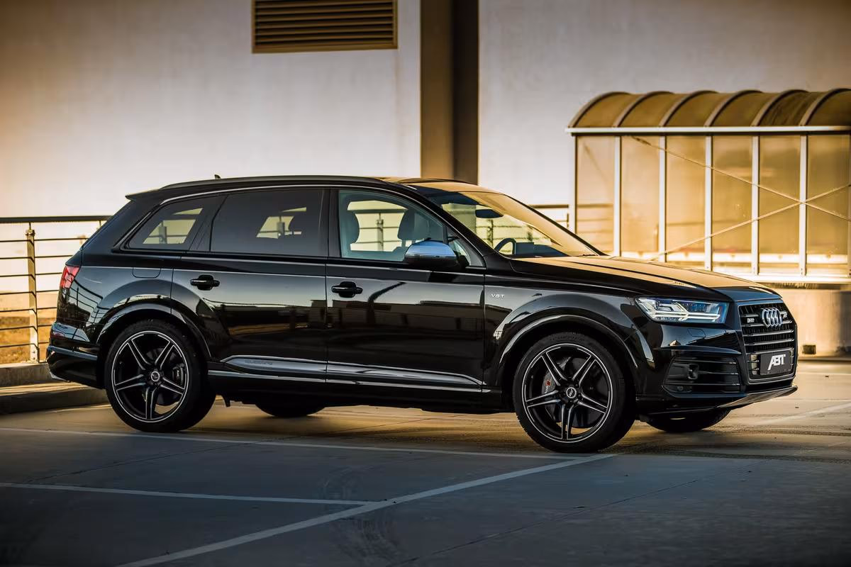 Schwarzer Audi Q7 mit ABT-Logo im Seitenprofil vor moderner Architektur.