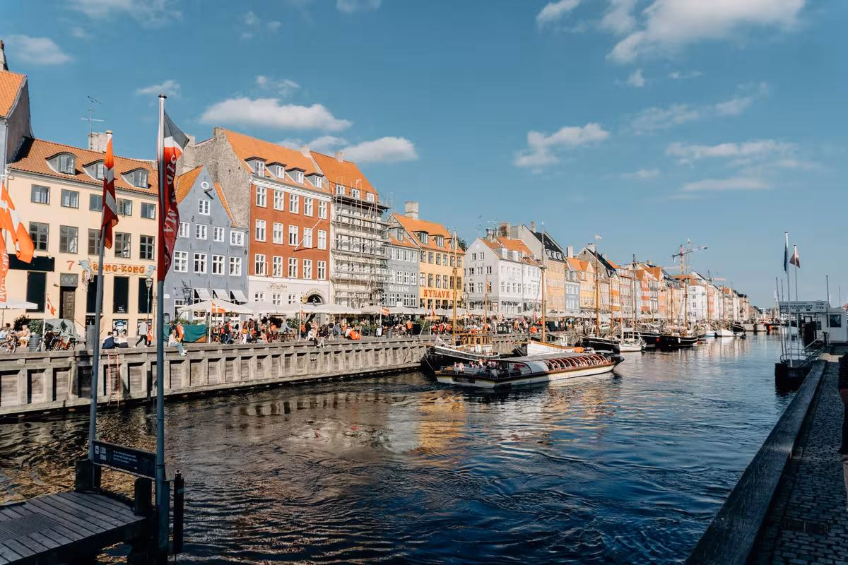 Copenhagen: Bunte Häuser am Hafen mit Booten und Menschen unter blauem Himmel