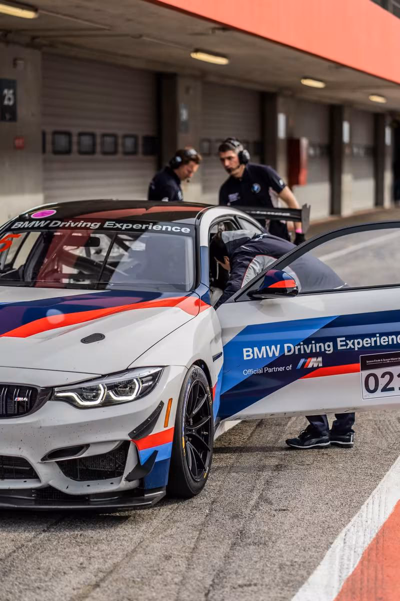 BMW M4 Rennwagen mit „BMW Driving Experience“-Livery im Boxenbereich.