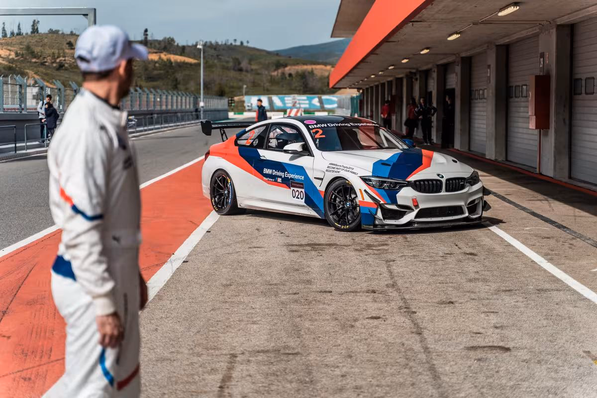 BMW Motorsport: BMW M240i Racing in der Boxengasse, Fahrer im weißen Rennoverall im Vordergrund.